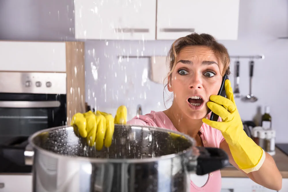 A woman in a kitchen calling a plumber to inspect her home's plumbing