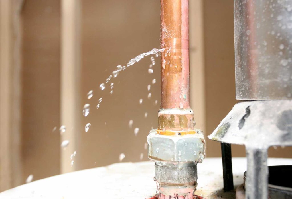 Water leaking from a damaged copper pipe connection during an emergency plumbing repair.