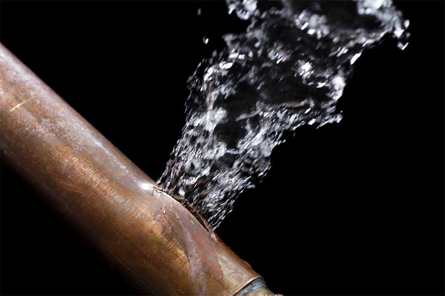 Water spraying from a burst copper pipe during an emergency plumbing leak.