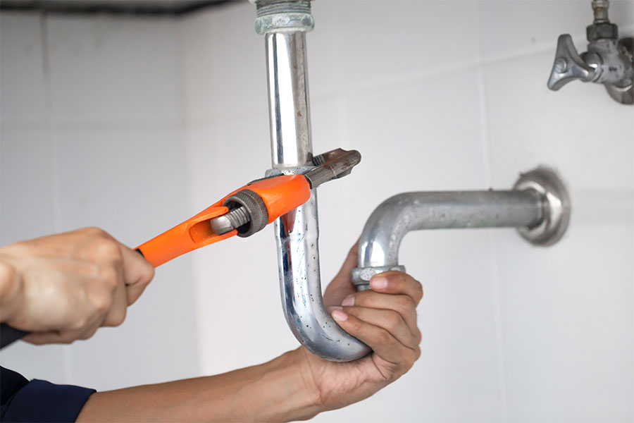 Plumber tightening a metal sink drain pipe with a pipe wrench during plumbing repair.